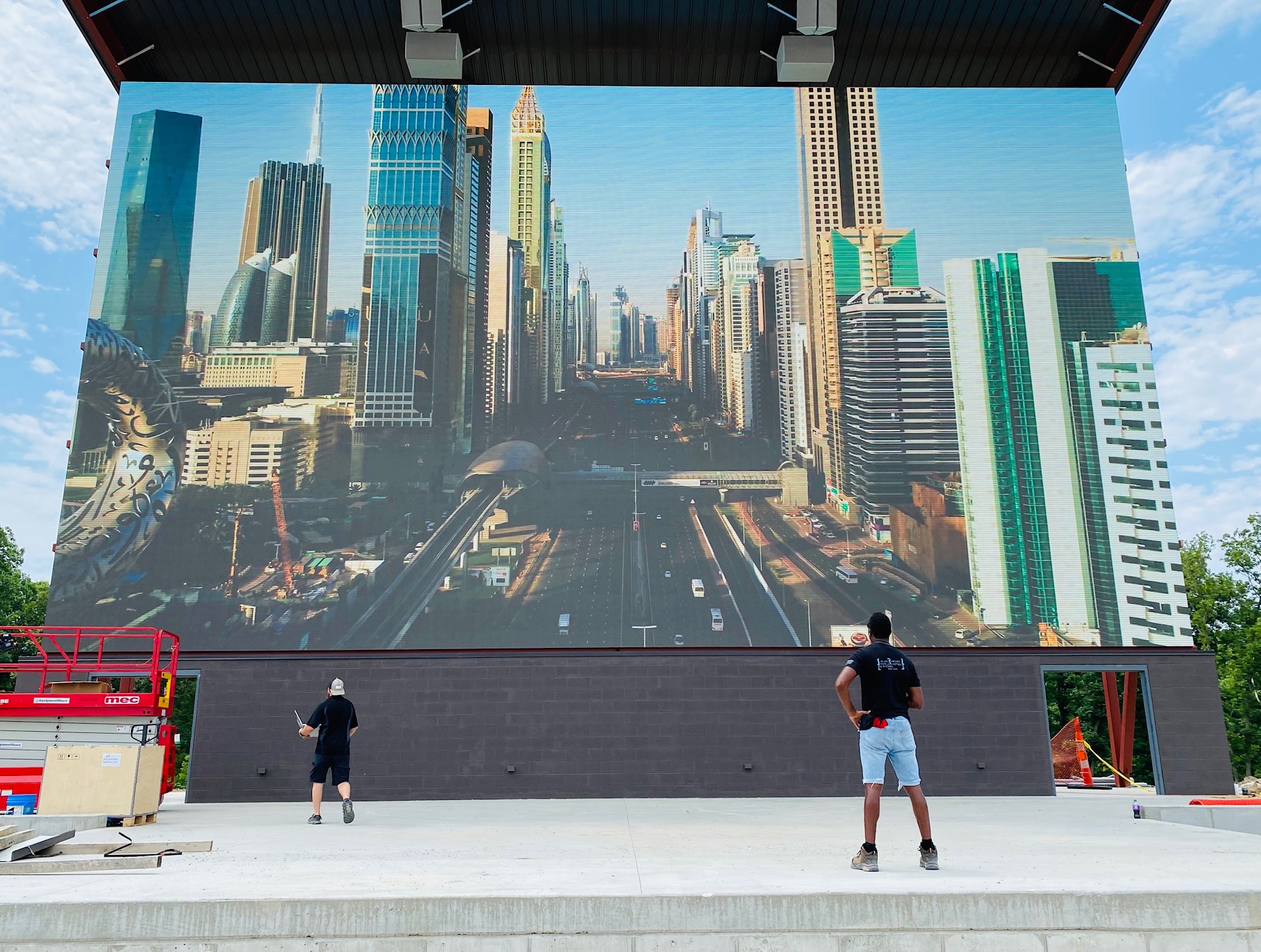 men gazing at an led wall display set up outside and it is showing a city street